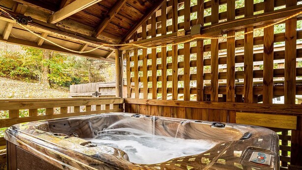 Un jacuzzi bajo una pérgola de madera, con una valla de madera al fondo.