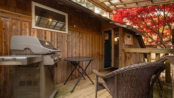 A wooden deck with a grill, a table, and a wicker chair.