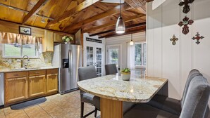 A kitchen with wooden cabinets, a stainless steel refrigerator, a granite countertop, and a dining area with a bench and table. - Cozy Cottage - Perfect Private Getaway. (Hopwood)