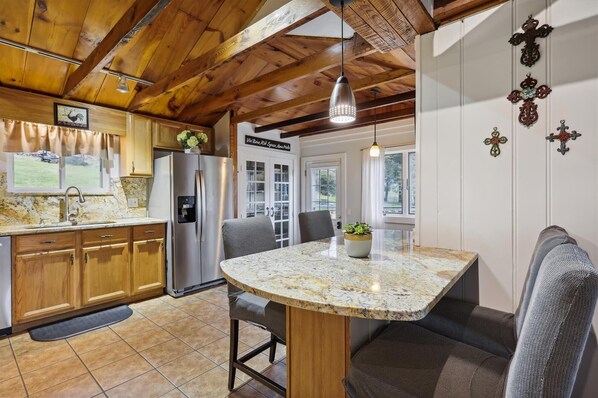 A kitchen with wooden cabinets, a stainless steel refrigerator, a granite countertop, and a dining area with a bench and table.