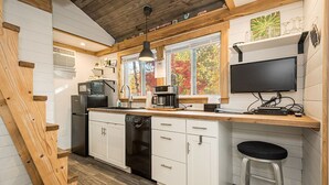 Una cocina moderna con armarios blancos, una encimera de madera, lavavajillas, cafetera y televisor montado en la pared.