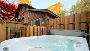 Un jacuzzi en un patio trasero con un porche de madera y una casa al fondo.