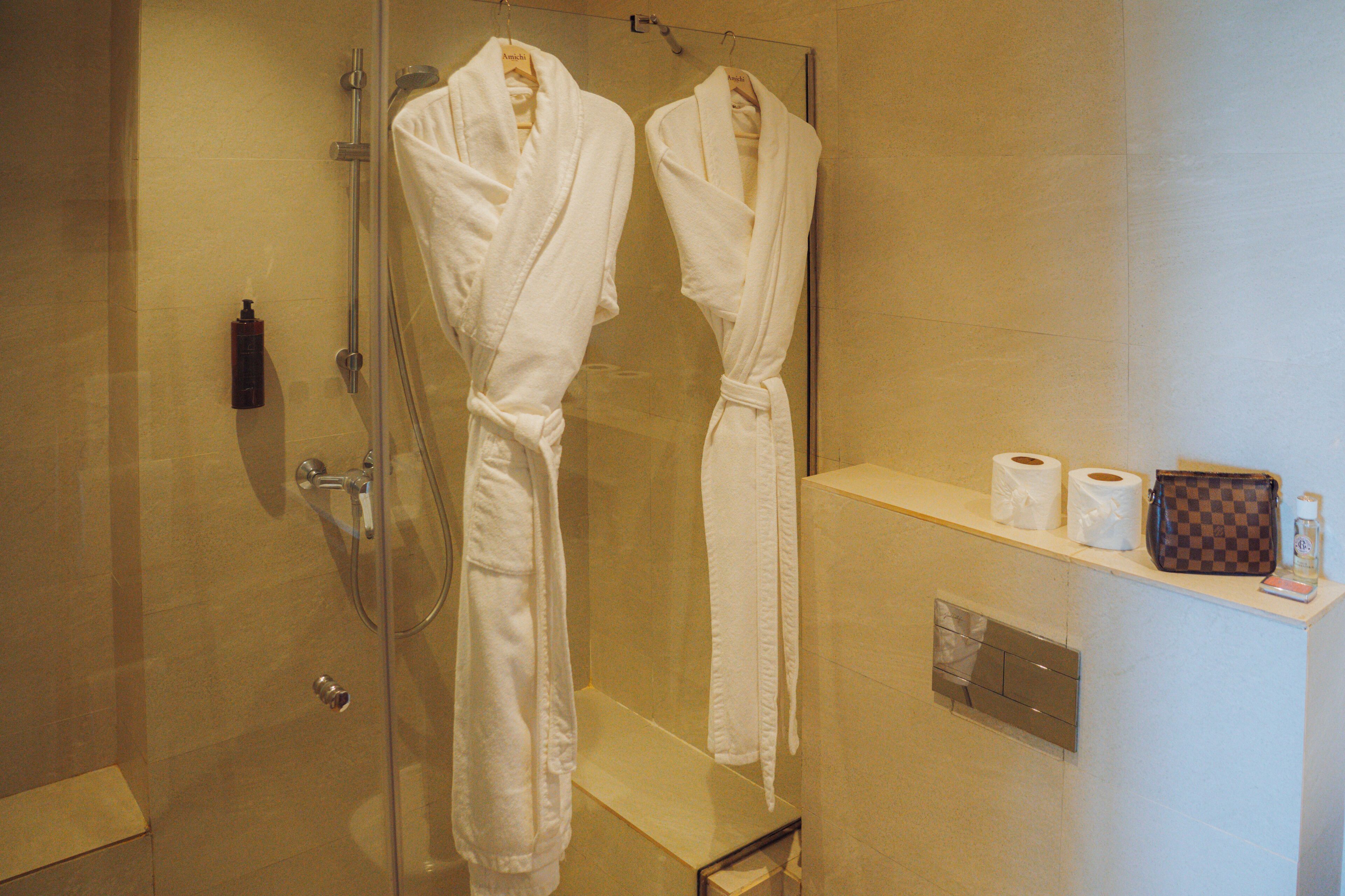 Une salle de bain avec deux peignoirs blancs suspendus, une douche en verre et des articles de toilette rangés sur une étagère.