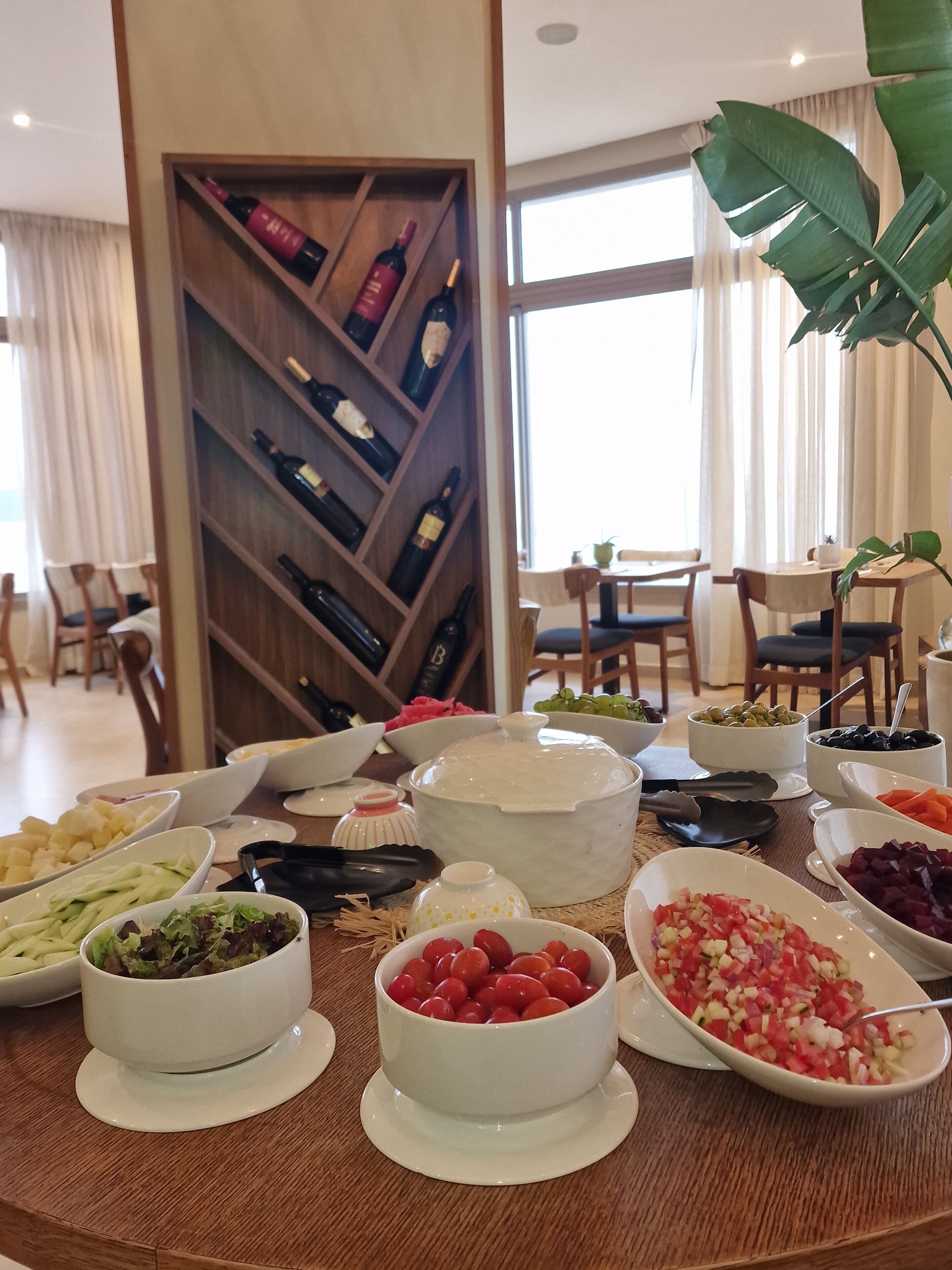 A dining table with various food items and a wine rack in the background.
