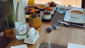 A table with a meal set, a bottle of Sidrol, and a view of the beach and water.