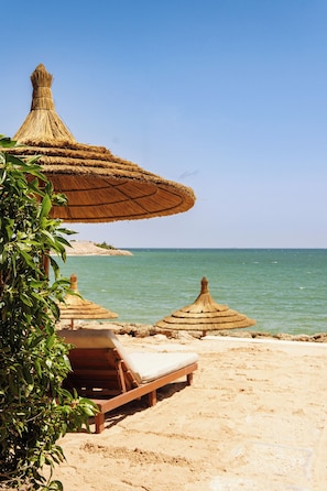 A beach with thatched umbrellas and wooden lounge chairs. - Dakhla South Bay, WorldHotels Distinctive (Dakhla)