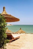 Una playa con sombrillas de paja y sillones reclinables de madera.