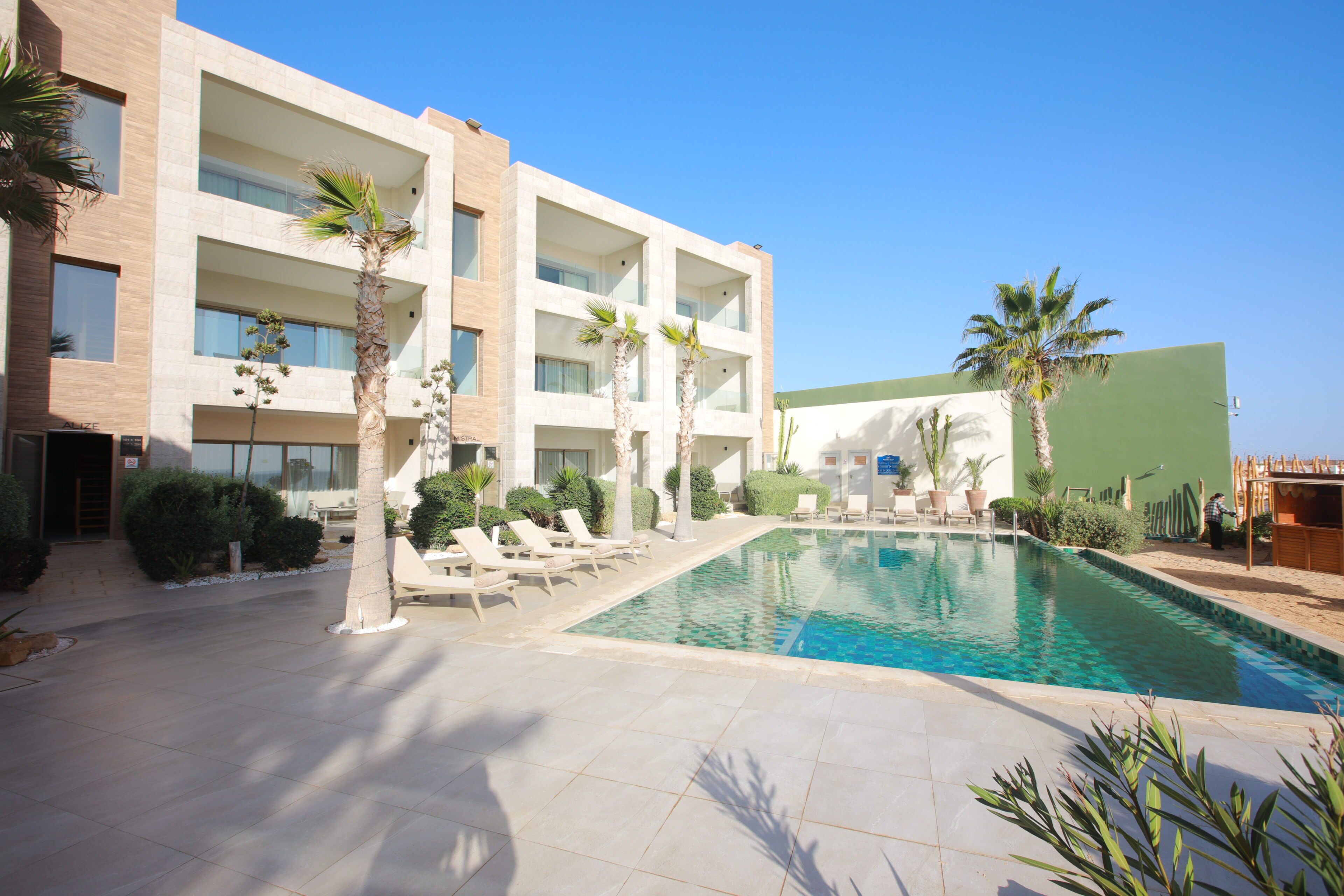 A hotel with a swimming pool, multiple balconies, and palm trees.