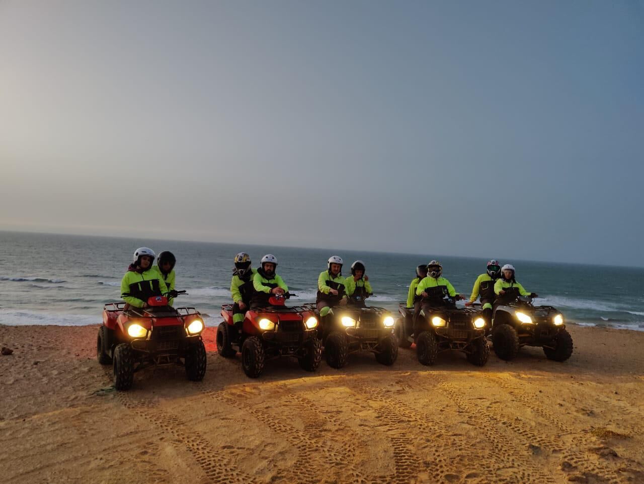 Four people on ATVs on a beach at dusk.