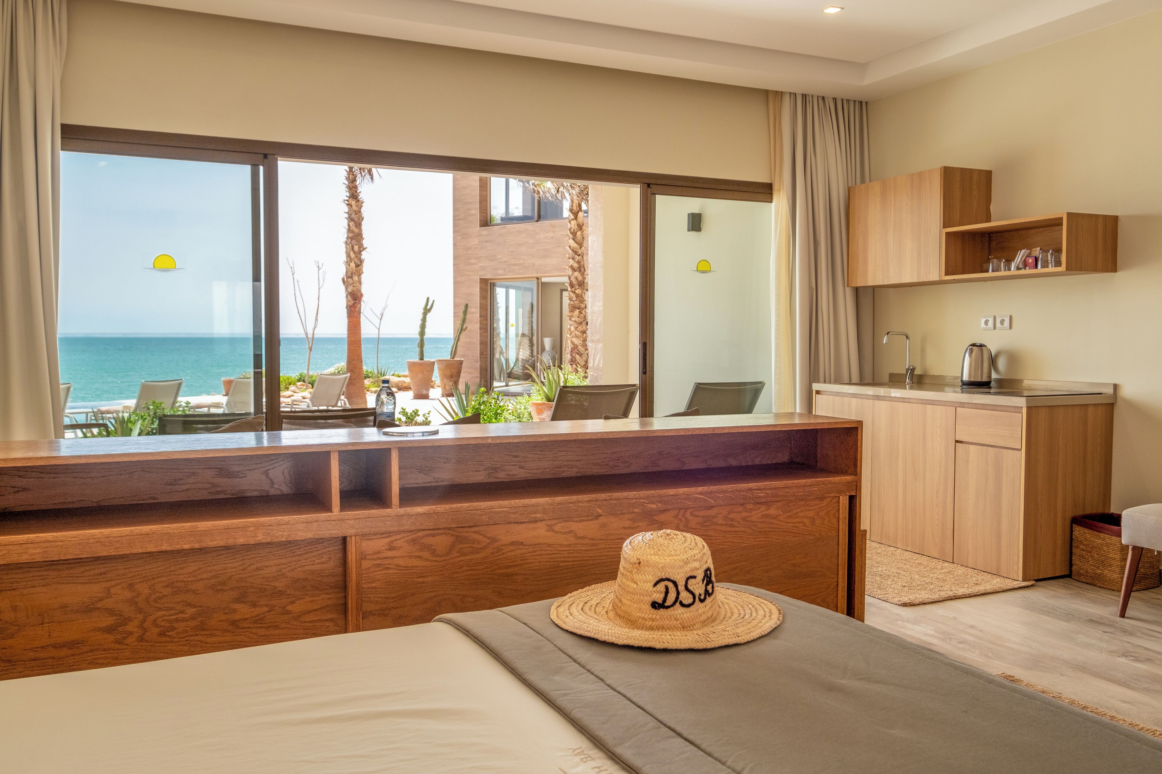 Habitación de hotel con vista al mar, un escritorio de madera, un sombrero y una kitchenette.