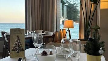 A dining table set for two with a view of the ocean, a small Christmas tree, and a candle holder.