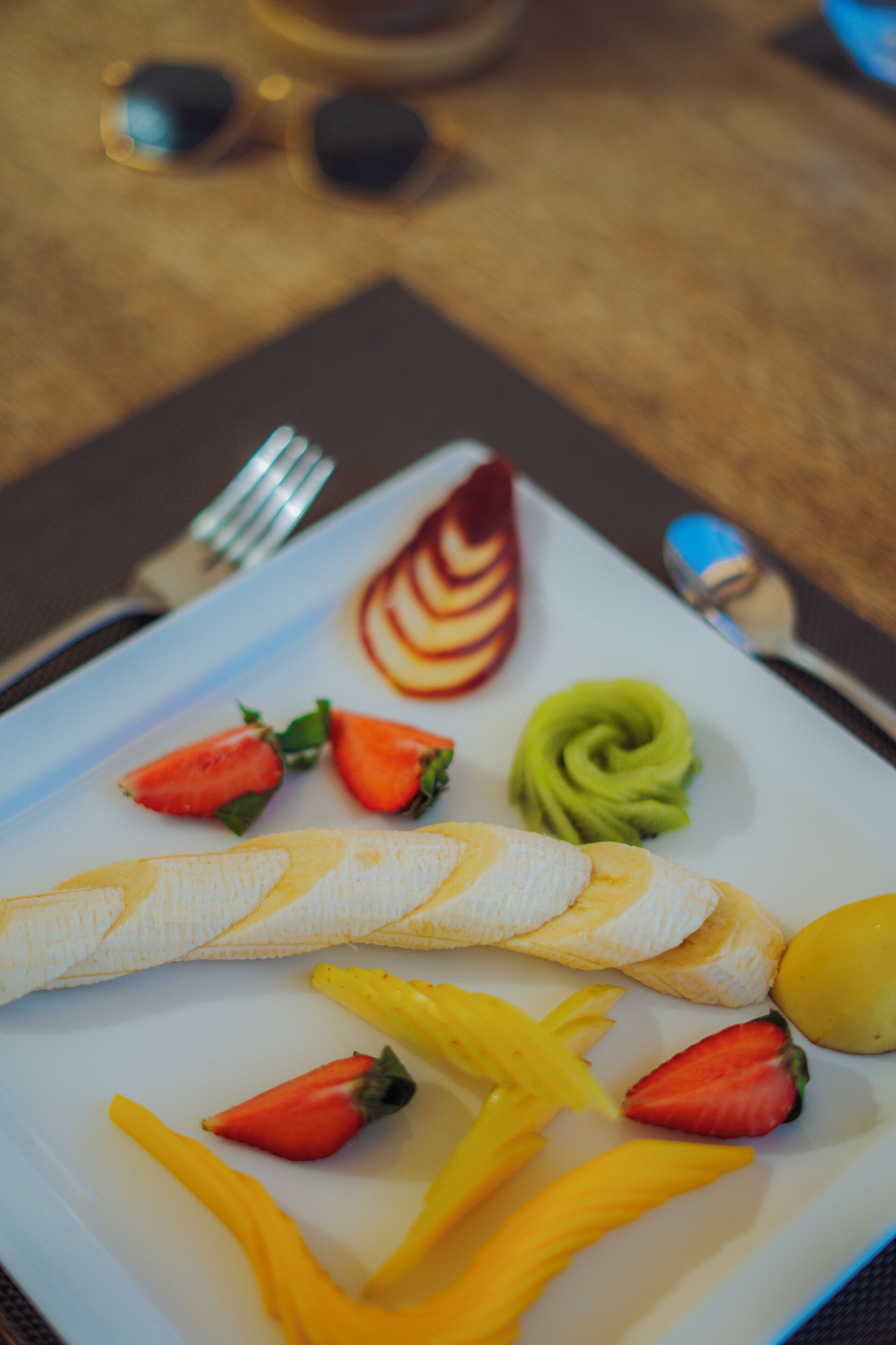 Une assiette contenant des fruits et une banane, une cuillère et une fourchette, le tout posé sur une table.