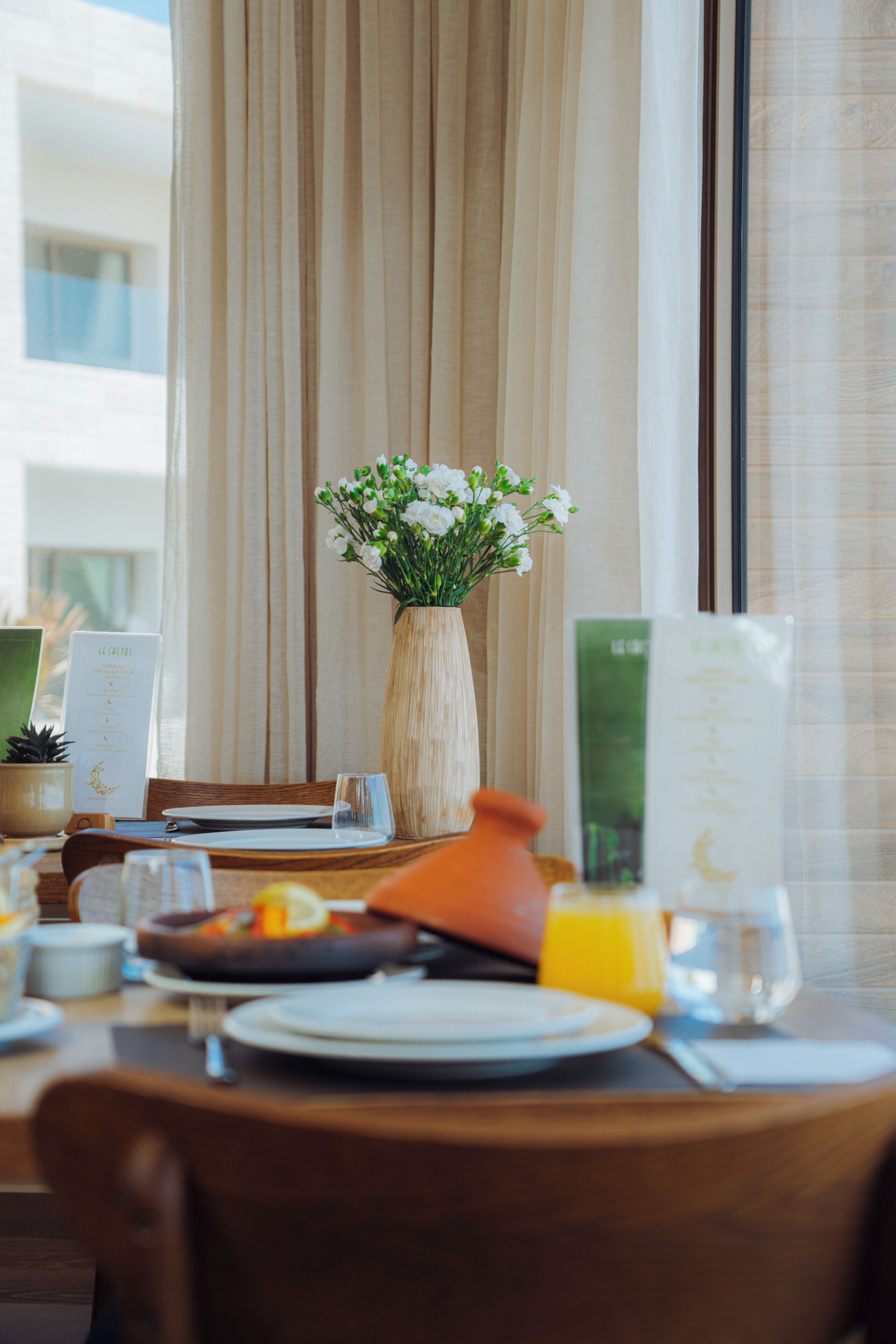 Une table à manger ornée d’un vase de fleurs, d’un menu et d’un verre de jus d’orange.