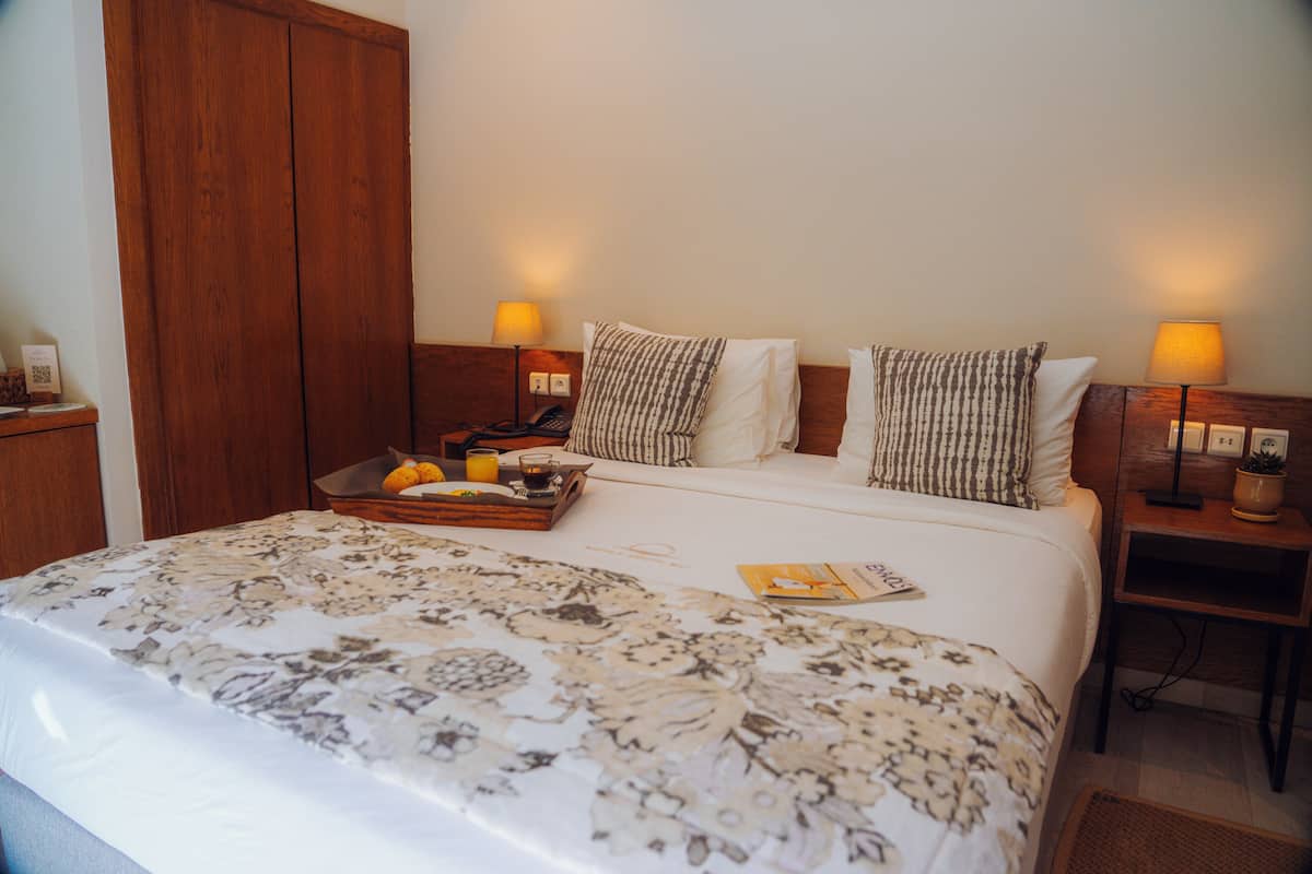 A hotel room with a large bed, two bedside lamps, a wooden wardrobe, and a tray with breakfast items.
