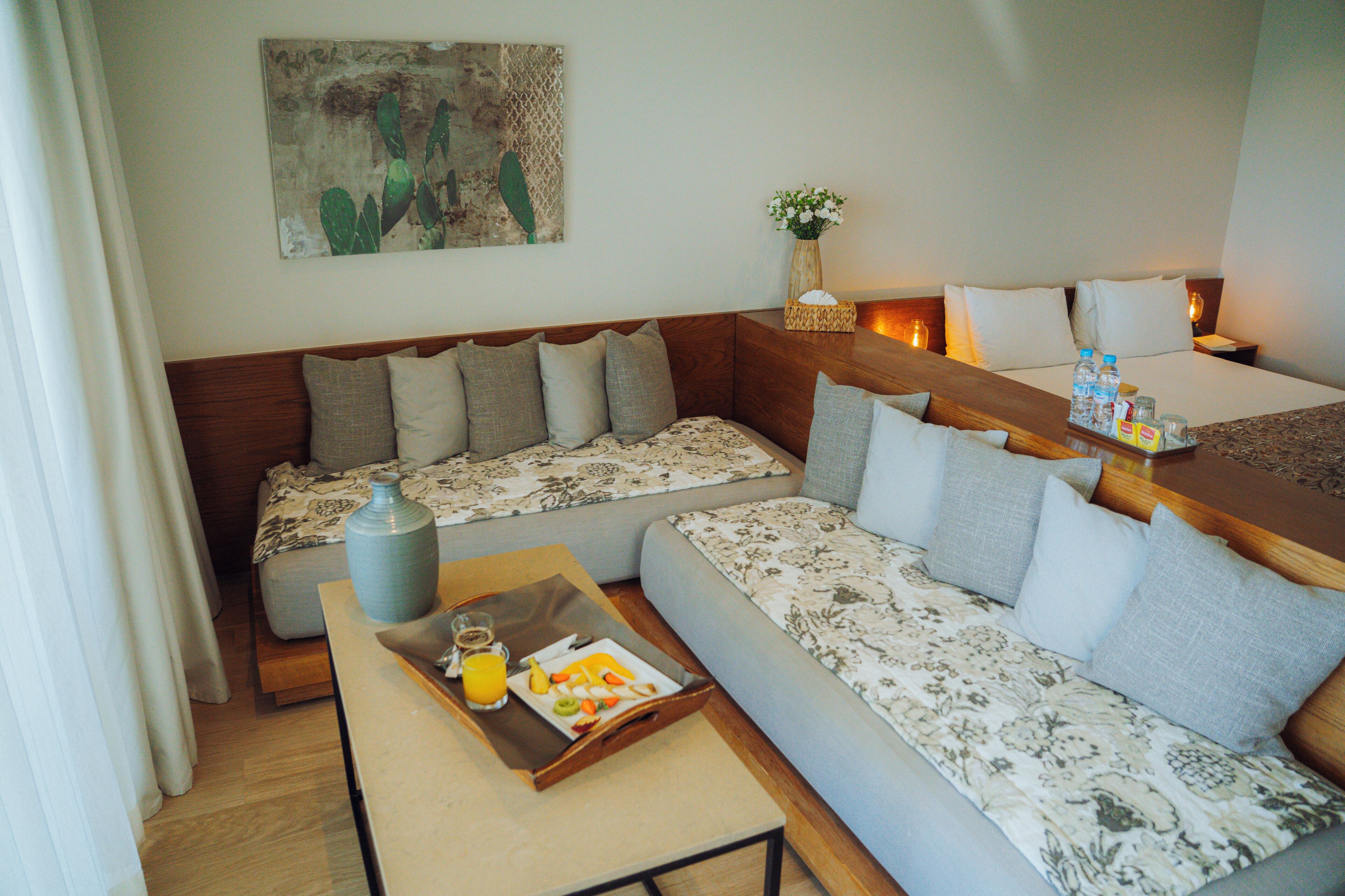 Une chambre d’hôtel avec un canapé, une petite table avec un plateau de petit-déjeuner, un vase de fleurs et un tableau au mur.
