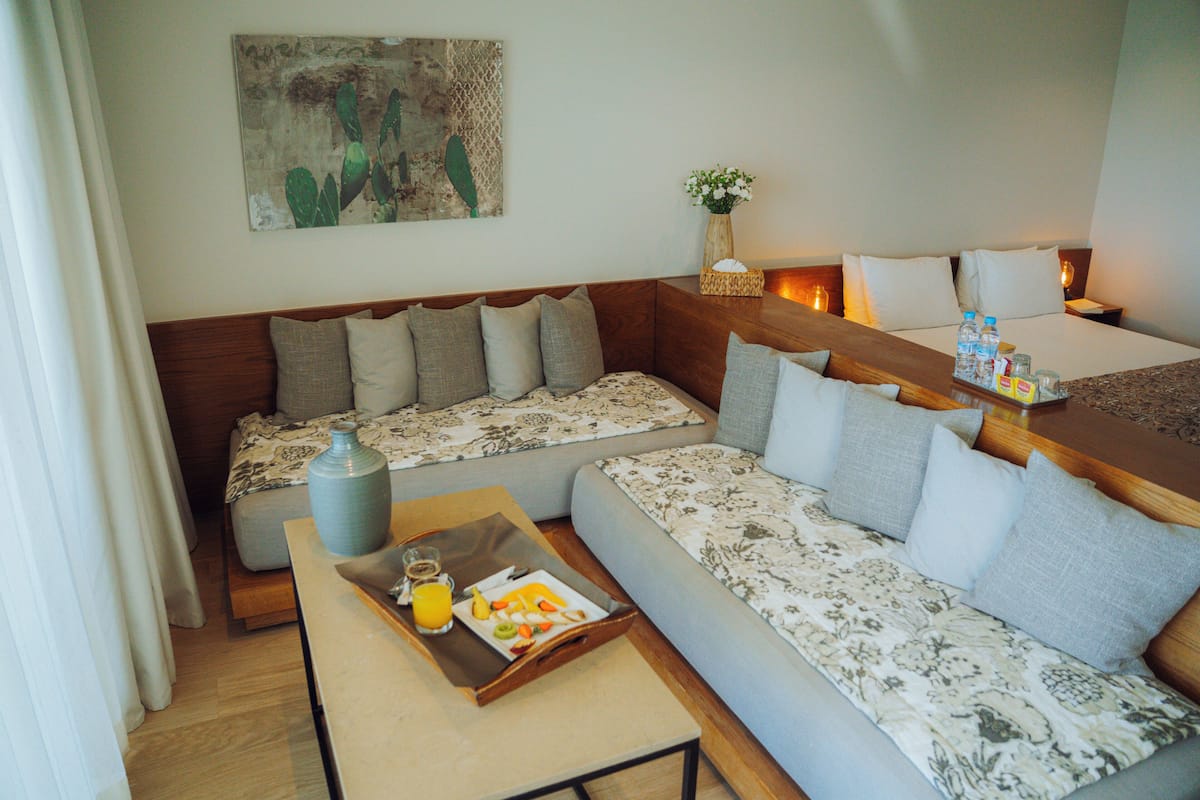 Une chambre d’hôtel avec un canapé, une petite table avec un plateau de petit-déjeuner, un vase de fleurs et un tableau au mur.