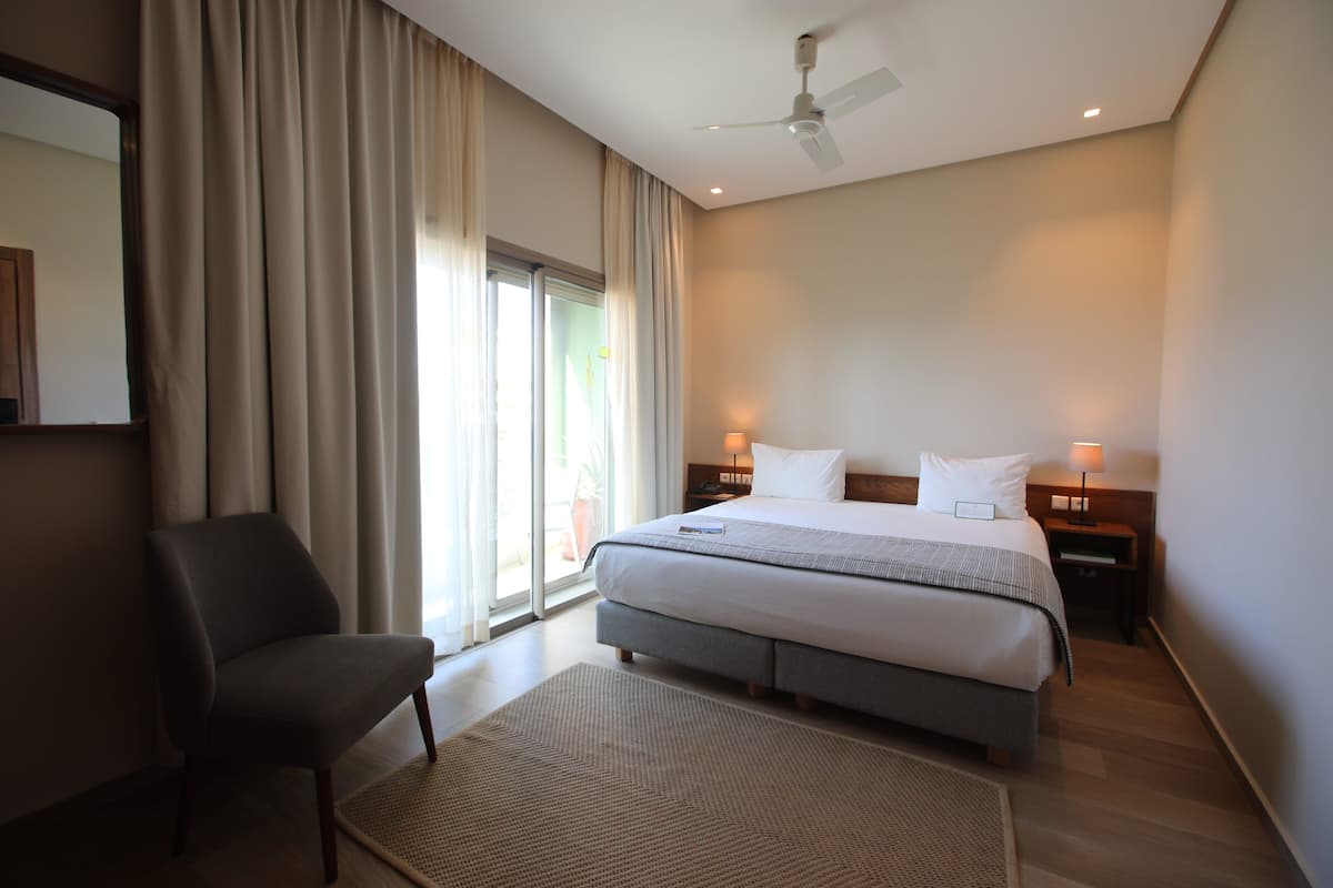 A hotel room with a bed, a chair, a ceiling fan, and a window with curtains.