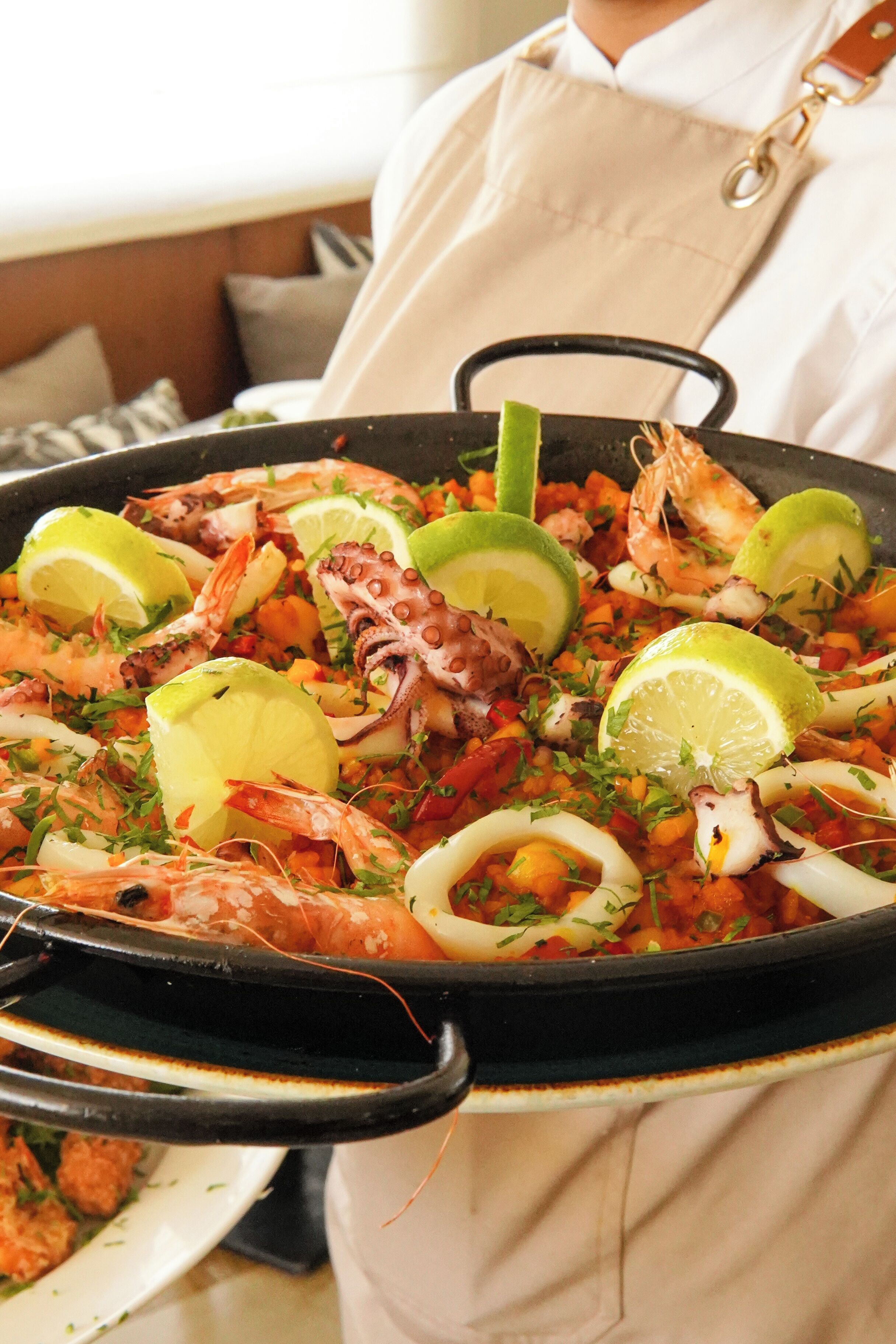 A large black pan filled with seafood, including shrimp and squid, garnished with lime and herbs.