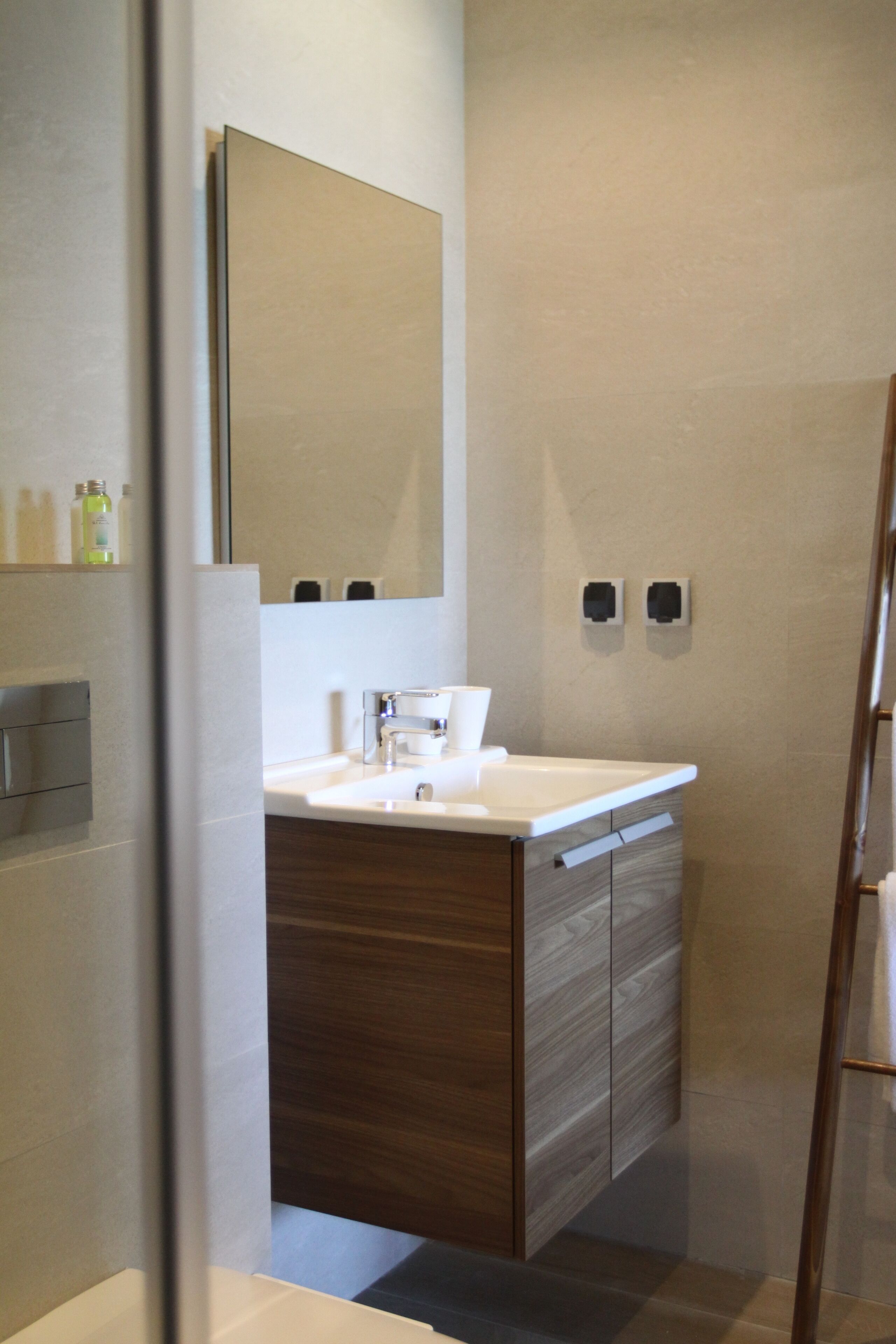 Un baño moderno con lavamanos blanco, tocador de madera y un espejo grande.