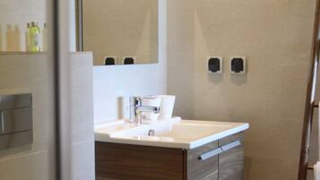 Un baño moderno con lavamanos blanco, tocador de madera y un espejo grande.