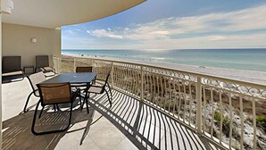 A balcony with a table and chairs, overlooking a beach. - Dunes of Crystal Beach 104 | Free Seasonal Beach Service & More! (Destin)