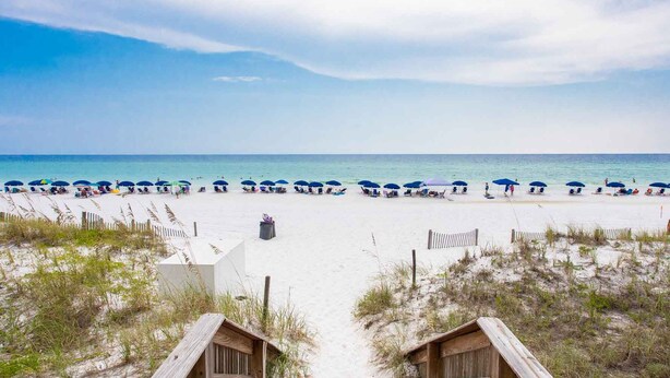 A beach with a wooden boardwalk leading to a sandy beach area with umbrellas and beach chairs. - Dunes of Crystal Beach 104 | Free Seasonal Beach Service & More! (Destin)