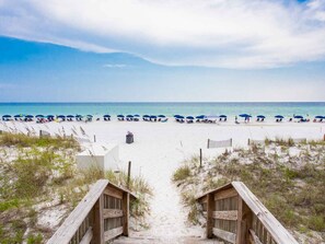 A beach with a wooden boardwalk leading to a sandy beach area with umbrellas and beach chairs.