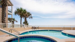 A pool area with two circular pools, a lounge with chairs, and palm trees. - Dunes of Crystal Beach 104 | Free Seasonal Beach Service & More! (Destin)