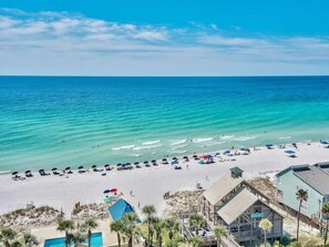A beach with clear turquoise waters, a sandy shore, and a few buildings including a structure with a green roof.