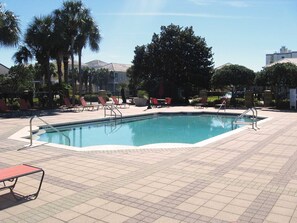 A rectangular pool with a tiled deck, surrounded by palm trees and red lounge chairs.
