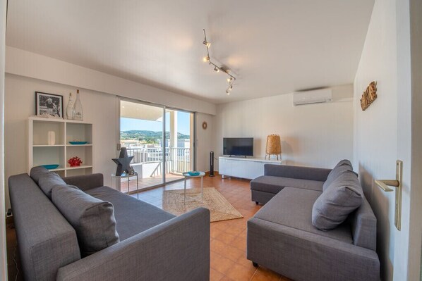 A modern living room with grey sofas, a flat-screen TV, and a balcony with a view. - Apt With Pool 10 Min From The Beach (Sainte-Maxime)