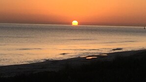 Auringonlasku rannan yllä, jossa vesi on tyyntä ja horisontti kaukana.