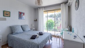 Un dormitorio con cama, escritorio, silla, ventana con cortinas y balcón.