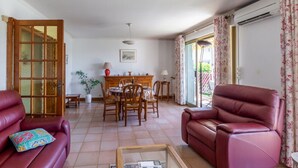 Una sala de estar con un sofá de cuero rojo, una mesa de comedor con sillas y un amplio ventanal con cortinas.