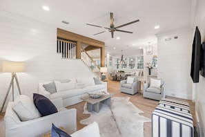 A modern living room with a white sofa, striped armchairs, a coffee table, and a staircase leading to another level.