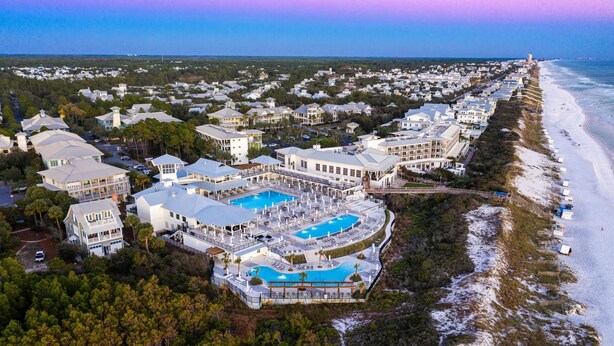 An aerial view of a resort with multiple buildings, a large swimming pool, and a beach.