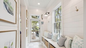 A hallway with a bench, framed pictures, and a door leading outside.