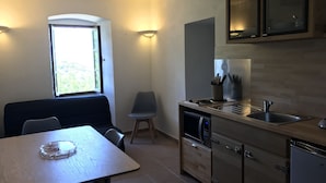 A compact kitchen with a dining table, chairs, a microwave, a dishwasher, and a window providing natural light. - Maison de Village Avec vue Imprenable sur le Cap Corse (Santa-Reparata-Di-Balagna)