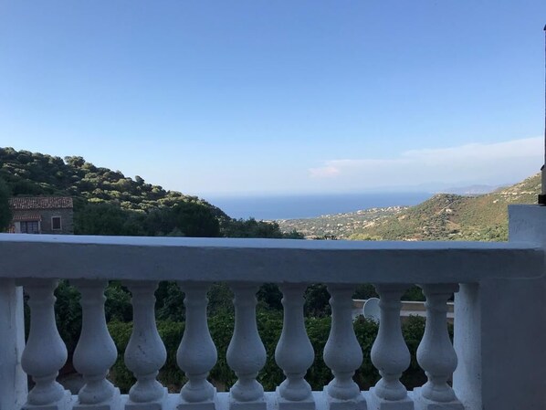 A balcony with a white balustrade overlooking a hilly landscape and the sea.