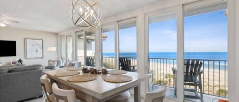 A dining area with a large table, chairs, and a view of the beach.