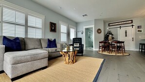 A living room with a grey sofa, a glass coffee table, and a dining area with wooden chairs and a table.