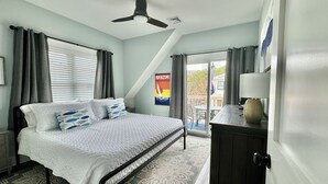 A bedroom with a bed, a ceiling fan, a poster, and a view of the outside.