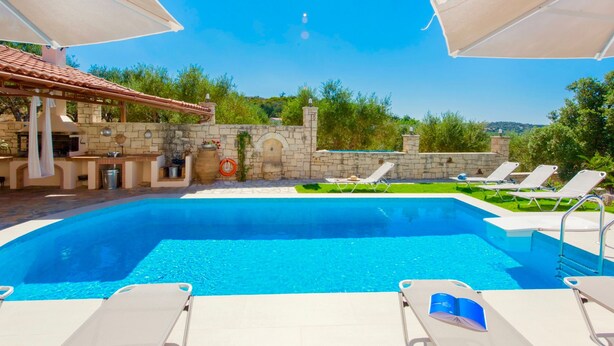 A swimming pool with lounge chairs and umbrellas, a stone wall, and a barbecue area. - Villa Korini Crete (Mylopotamos)