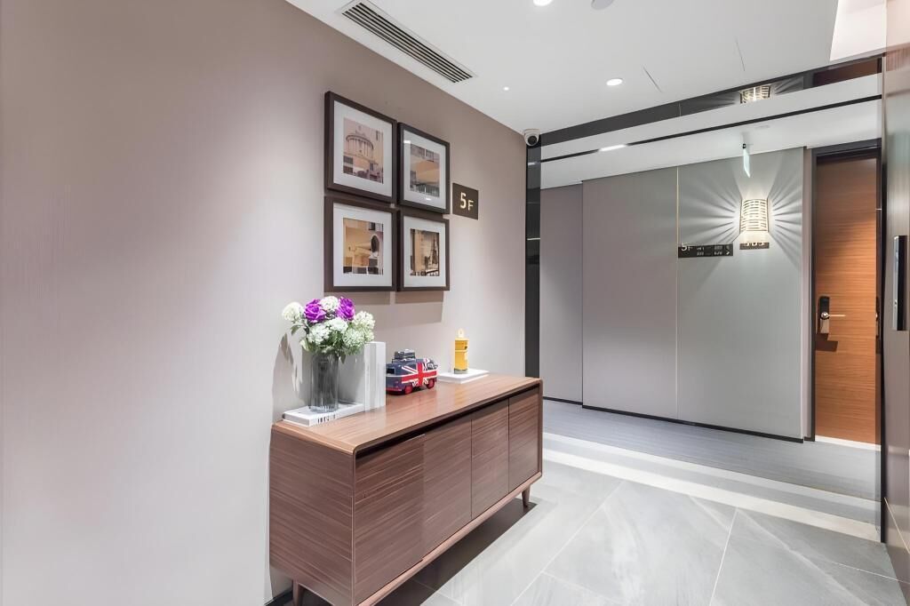 A modern reception area with a wooden reception desk, framed pictures on the wall, and a digital display above the door.