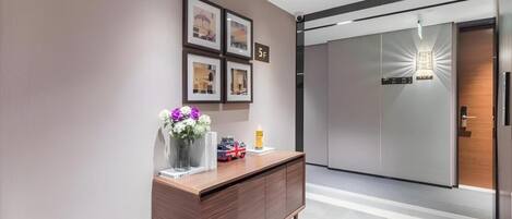 A modern reception area with a wooden reception desk, framed pictures on the wall, and a digital display above the door.