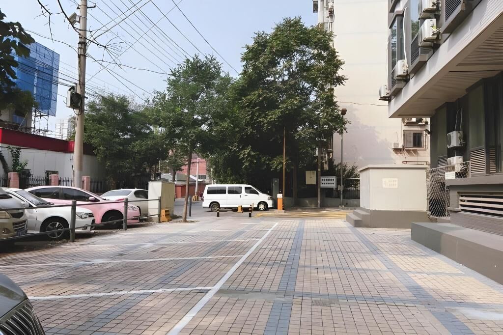 Un estacionamiento con autos y una camioneta blanca, rodeado de edificios y árboles.