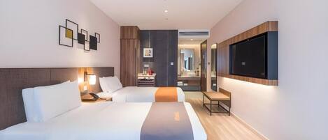 A modern hotel room with two beds, a TV, a desk, and a bathroom visible through an open door.