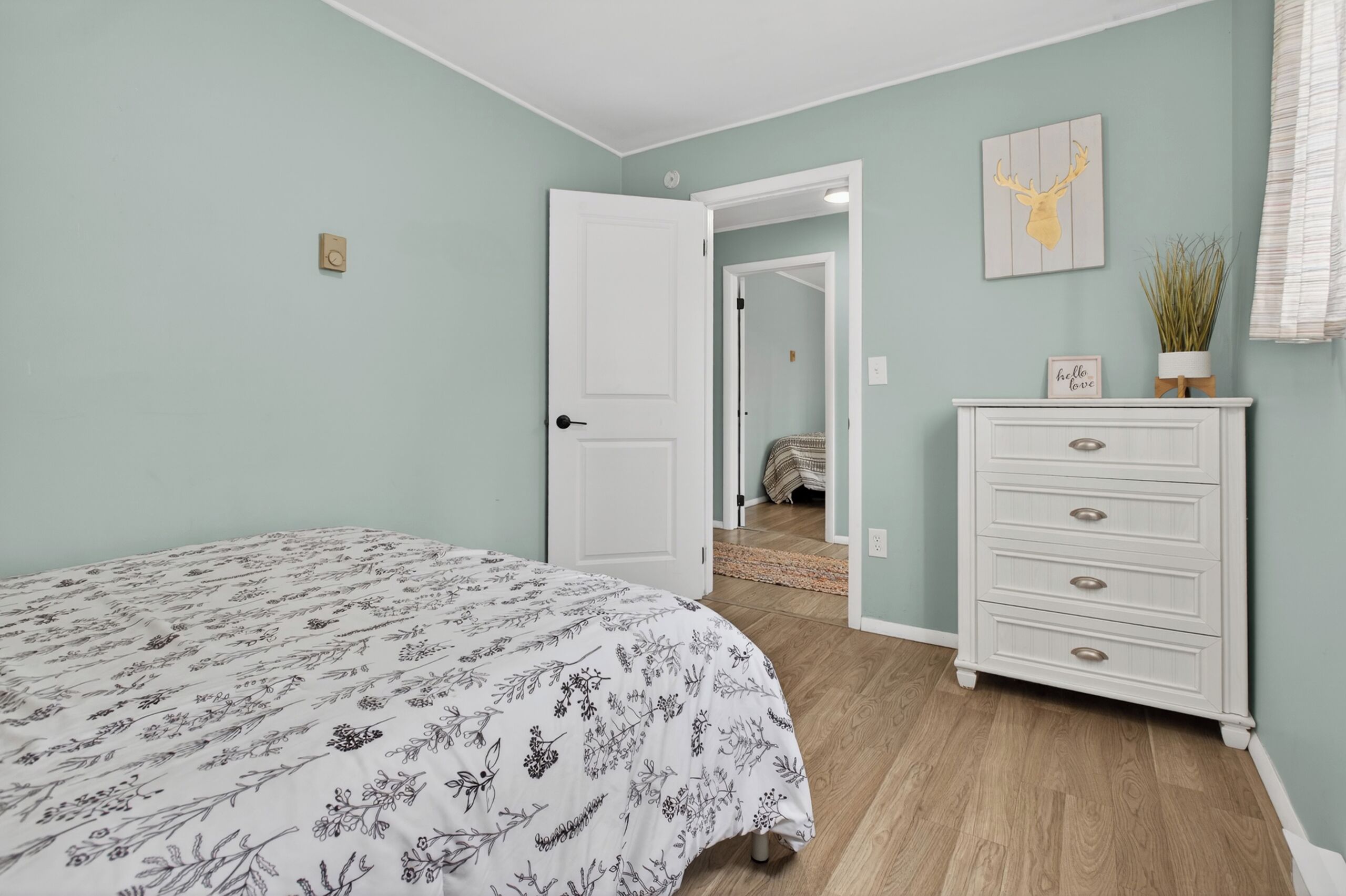 A bedroom with a bed, a dresser, a door, and a hallway leading to another room.