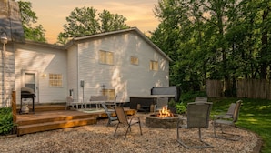 Ein Haus mit einer Terrasse, die einen Feuerkorb, Sitzgelegenheiten und einen Grillplatz bietet.