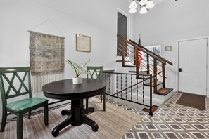 Un coin repas avec une table ronde et des chaises, un escalier avec une rampe en bois et un tapis à motifs sur le sol.